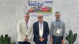Foto de três servidores do TCE/SC durante o ENCCO 2024. Da esquerda para a direita, Paulo Salum, o conselheiro Wilson Wan-Dall e Edson Biazussi. Eles estão em pé, um ao lado do outro, em frente a um painel com o logo do evento. Todos sorriem. 